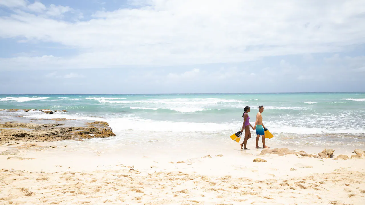 Couple carrying snorkeling gear while walking along the beach at Hyatt Zilara Rose Hall in Jamaica.