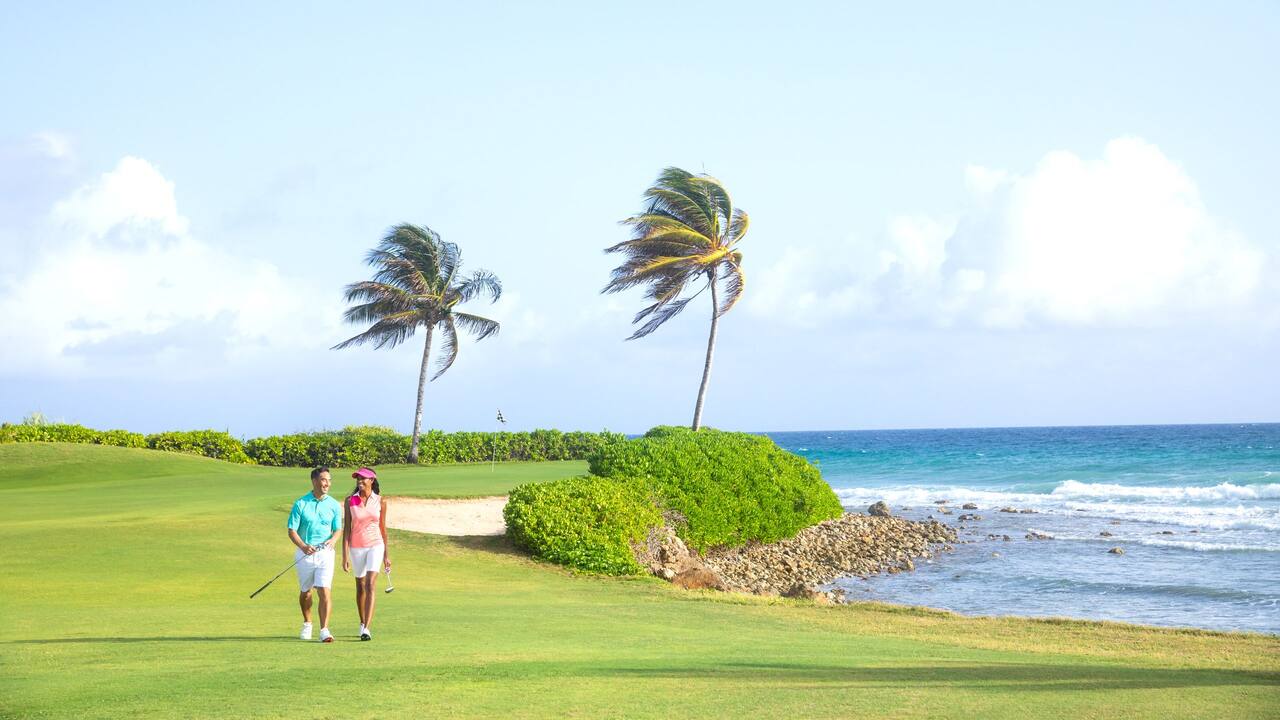 Couple walking along an oceanfront golf course near Hyatt Zilara Rose Hall with Caribbean Sea views.