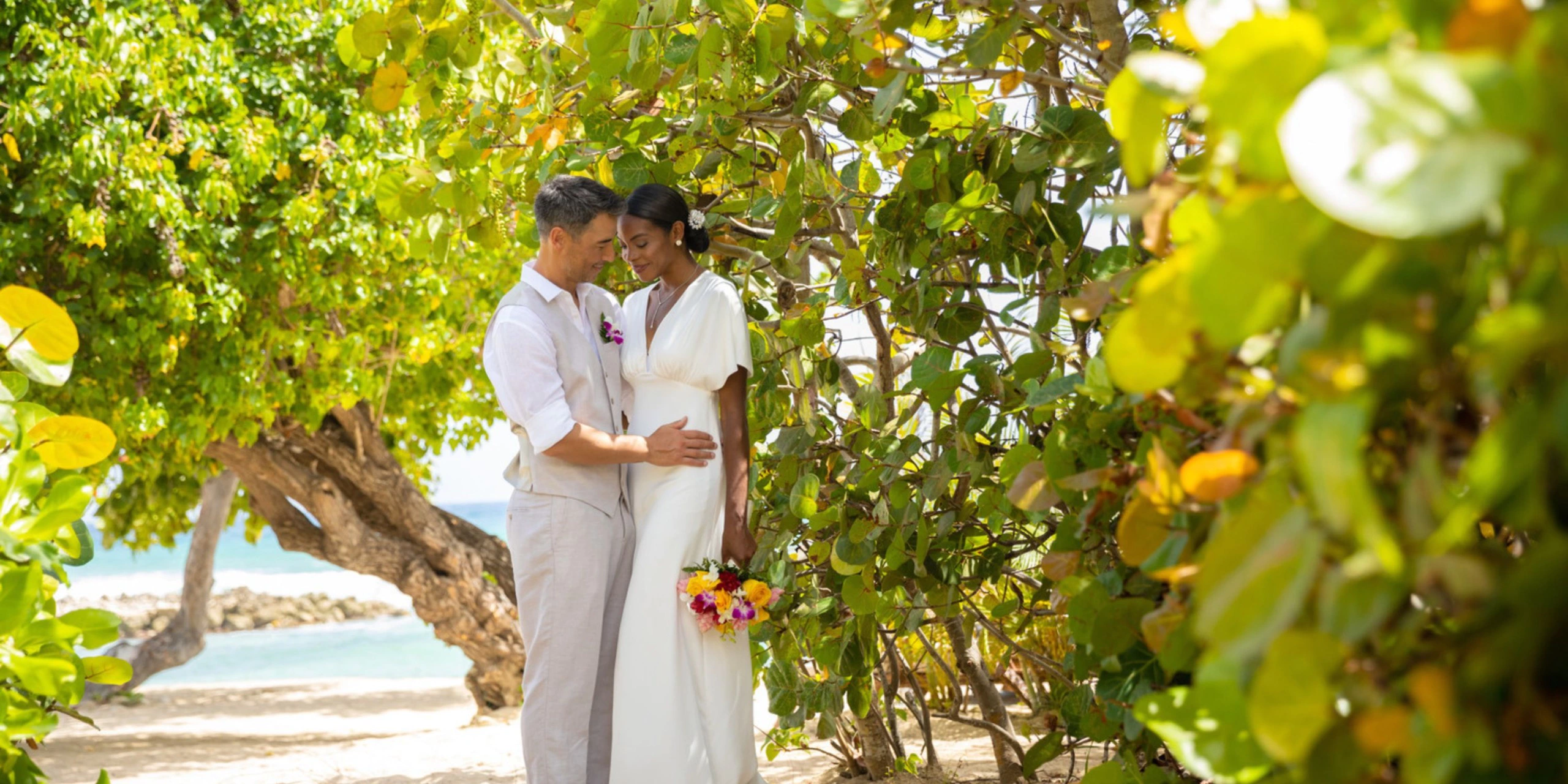Newlywed couple posing beneath tropical trees near the beach at Hyatt Zilara Rose Hall.